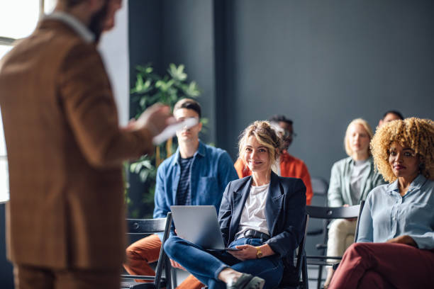 Group of Cheerful People on a Seminar Group of men and women sitting and listening to a seminar. They are smiling. training course stock pictures, royalty-free photos & images