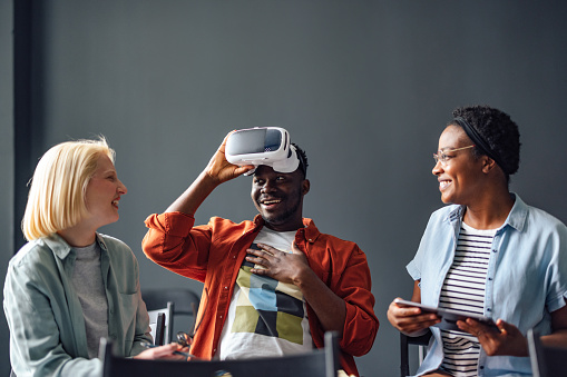 Two women smiling while their male friend is taking off virtual reality goggles. He is excited and happy.