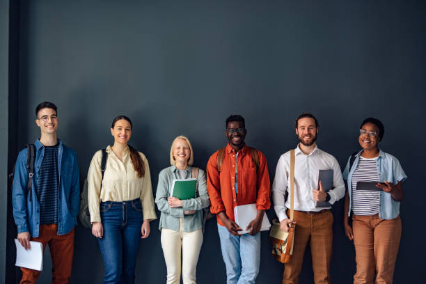 Group of Students Posing for a Photo at the University Group of female and male students standing against the wall, holding books and notebooks and smiling. people in a row photos stock pictures, royalty-free photos & images