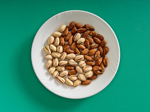 The yin and yang of mixed nuts, pistachios and almonds in harmony. The symbol on yin and yang peace and harmony represented with almonds and pistachios in a white plate on a green background.