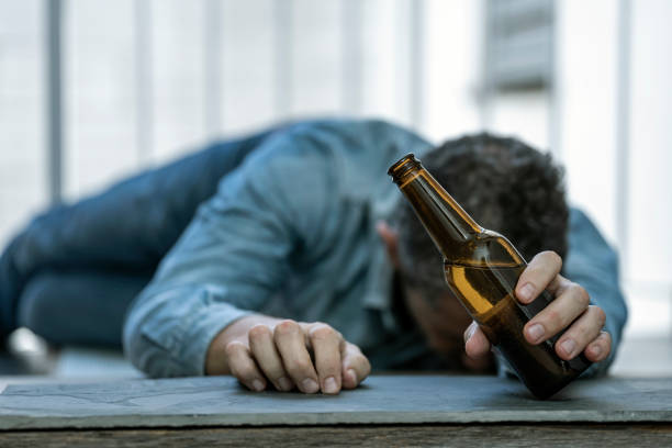 uomo ubriaco sdraiato sul pavimento addormentato con una bottiglia di birra in mano. dipendenza da consumo di alcol. concetto di alcolismo. focus selezionato. - alcoholism foto e immagini stock