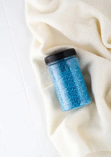 Package of blue glitter crystal salt on a bathroom beige towel. Jar of shimmering blue sea salt for home spa. Idea of relaxation, aromatherapy and self care. The effect of sea water on hair.