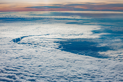 View from plane flying through clouds over the ocean on a sunny bright day.