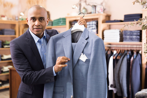 Friendly young adult male seller suggesting suit in clothing store