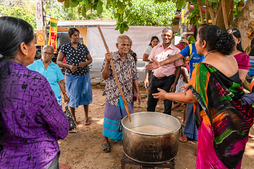 Hikkaduwa, Sri Lanka - November 18, 2019: Senior man is cooking food for people who are celebrating Gotabaya Rajapaksa winning the Presidential Elections on the street festival in the local community, and the crowd is watching.