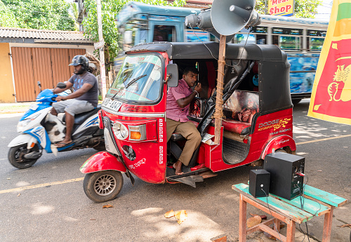 Hikkaduwa, Sri Lanka - November 18, 2019: People celebrate Gotabaya Rajapaksa winning the Presidential Elections on the street festival in the local community. Tuk Tuk motorized rickshaw tricycle taxi with sound equipment is providing music.