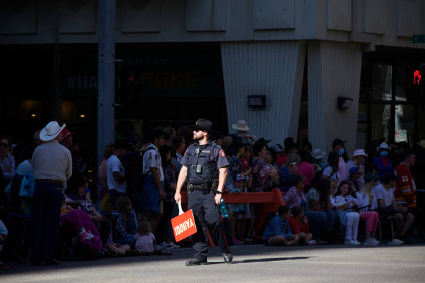 police patrolling Calgary city and lively with yahooo poster by stampede event poured black hat cowboy style Police man with beard café walking important avenue in the city center looking after old style black outfit cowboy hat red lines crowd waiting for parade dressed in a hat big children sitting on the ground in the shadow of classic black cowboy waiting for the opening of the stampede parade on july 07, 2022 large old-style buildings in the background orange barriers protection police station canada stock pictures, royalty-free photos & images