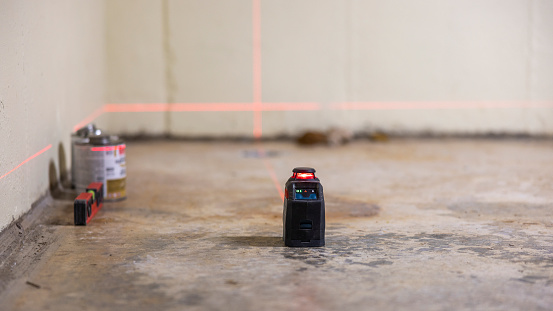 Installation of a radon mitigation system for house improvement by laser measurement in the basement. Selective focus on the foreground with defocused background.