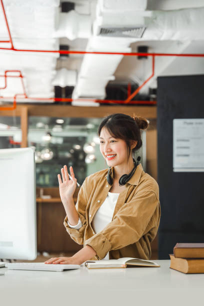 istock Young freelancer asian woman waving hello talking on video call, using laptop. 1408338529