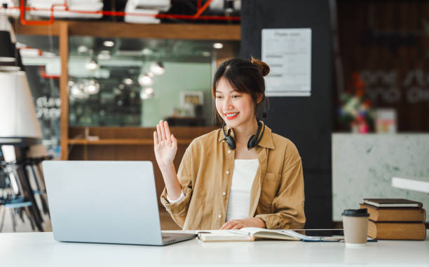 istock Young freelancer asian woman waving hello talking on video call, using laptop. 1408338533