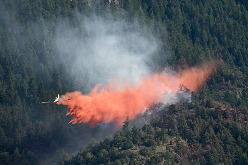 A twin engine aircraft takes off heading towards southern California fires seen in the background.