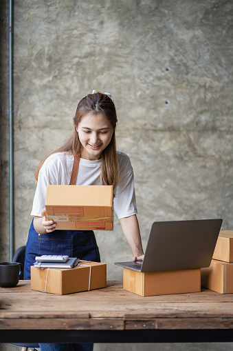 Asian woman working with box and laptop at home Starting an SME business, online selling ideas with parcel delivery. vertical picture