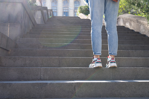 Tired woman in sneakers standing in front of long staircase with steps. Tourist walks around city concept