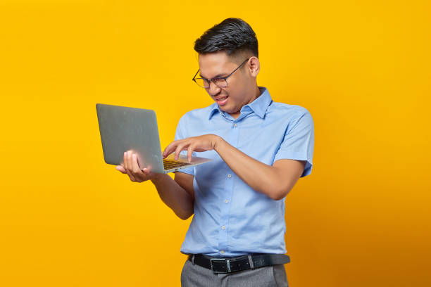 retrato de un joven asiático enojado con gafas usando una computadora portátil aislada sobre fondo amarillo. concepto de empresario y emprendedor - vertical caucasian glasses red hair fotografías e imágenes de stock