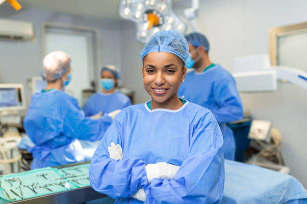 primer plano de una cirujana afroamericana mirando la cámara con colegas actuando en segundo plano en la sala de operaciones. el concepto de medicina - anestesista fotografías e imágenes de stock