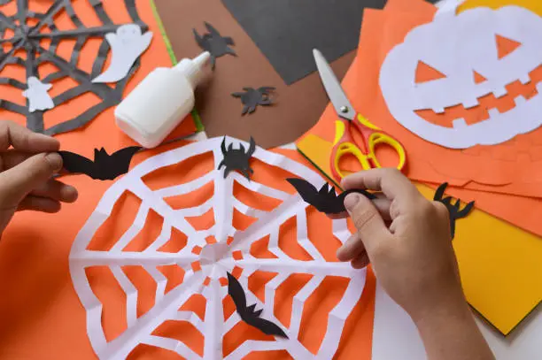 Photo of Close-up of children's hands that create paper crafts for Halloween. Homemade decorations for the holiday.