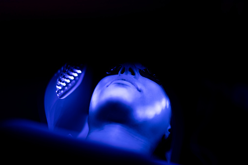 Young woman receiving UV light therapy on her face.