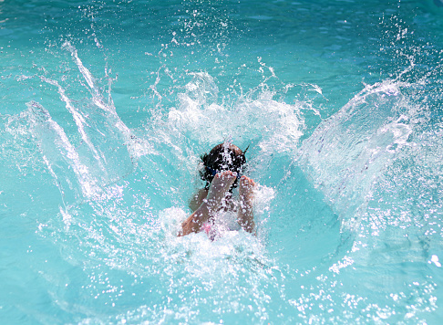 Stock photo showing close-up view of swimming pool with turquoise blue mosaic tiles lining the length of the pool.  Indian man swimming, splashing and playing in crystal clear water.