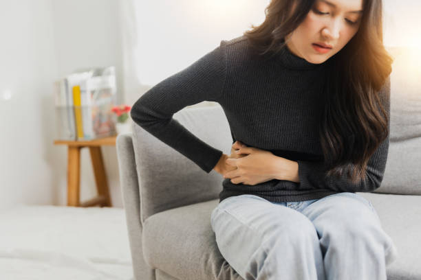 自宅でソファに座っている間に強い腹痛に苦しむ若い女性 - 月経前症候群 食事 ストックフォトと画像