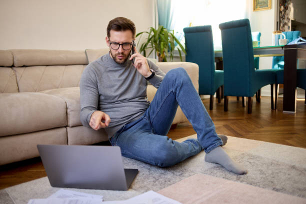 istock Mid adult man using his smart phone and laptop while working at home 1408370079