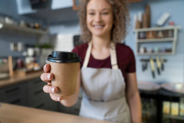 istock Young caucasian waitress passing dispensable cup towards the camera 1408370252