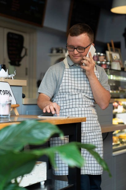 istock Young caucasian waiter with down syndrome using phone and digital tablet 1408371572
