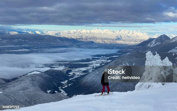 Young Snowboarder Stands Atop A Mountain And Observes The Breathtaking Landscape Stock Photo - Download Image Now