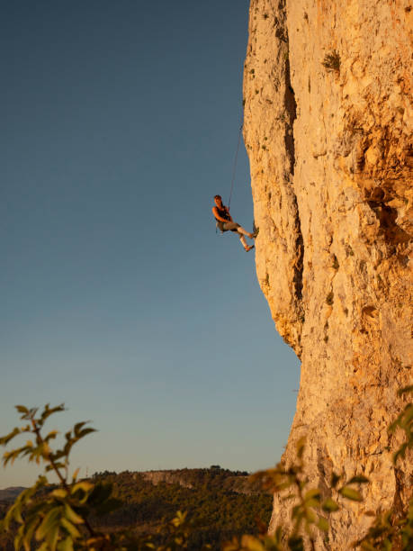 istock VERTICAL: Athletic female rock climber stops midway up a towering rocky cliff. 1408371812
