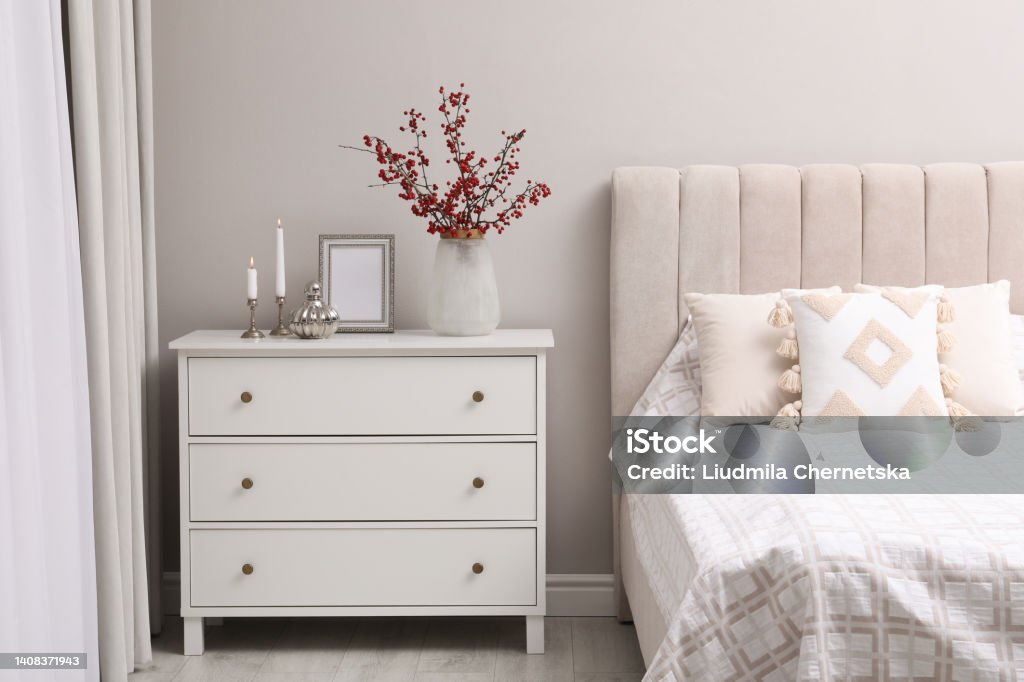 Hawthorn branches with red berries, candles and frame on chest of drawers in bedroom Dresser Stock Photo