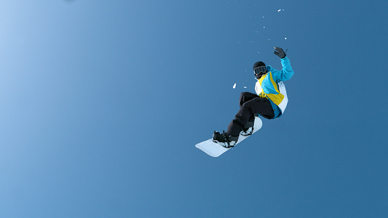 BOTTOM UP: Athletic male snowboarder does a spectacular grab trick high in the air. Unrecognizable man on winter vacation in Japanese mountains does an extreme trick while riding in the fun park.