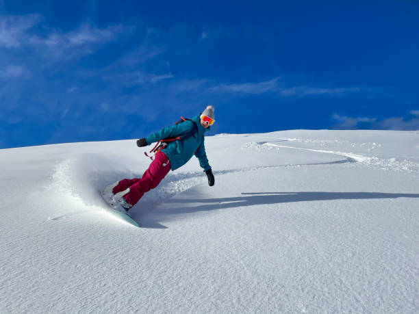 Cheerful female snowboarder sprays fresh powder snow while riding off-piste. Cheerful female snowboarder sprays fresh powder snow while riding off-piste in the beautiful Slovenian mountains. Woman on snowboarding vacation in Julian Alps smiles while shredding champagne powder. julian alps stock pictures, royalty-free photos & images