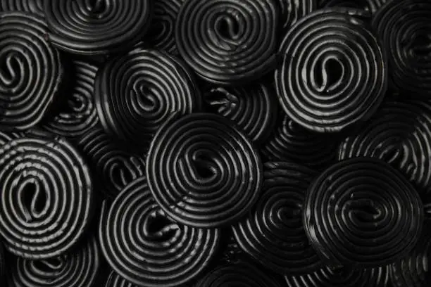 Tasty black liquorice candies as background, top view