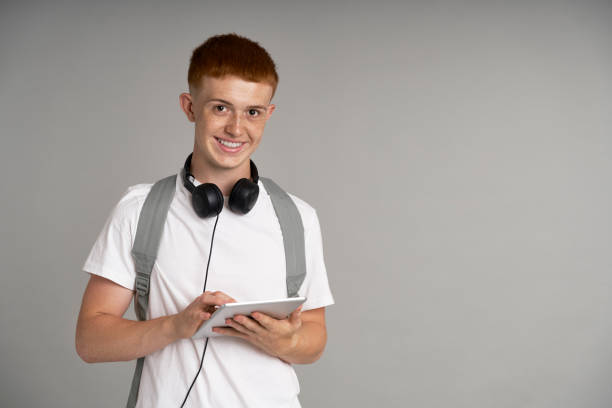 Ginger male student using digital tablet at grey background stock photo