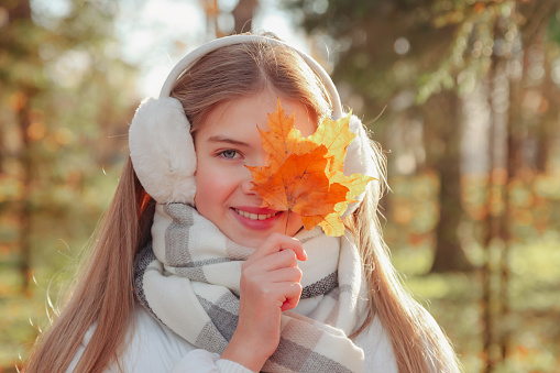 Portrait teenage girl with fall leaves looking at camera wearing casual clothes in an autumn park outdoors. Cute teen model walking in beautiful golden fall against background of nature. Copy space