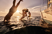 Carefree people jumping into sea from boat at sunset.