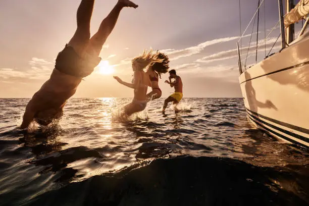 Photo of Carefree people jumping into sea from boat at sunset.