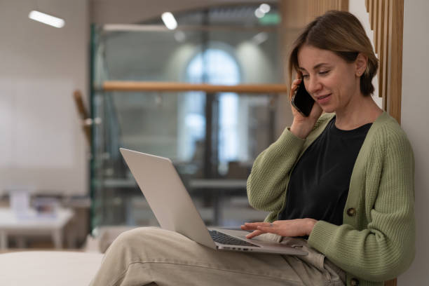 istock Serious businesswoman discussing project details via cellphone while working remotely on laptop 1408374664