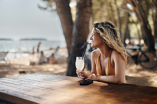 Young happy woman enjoying while drinking fresh lemonade on the beach in a café. Copy space.