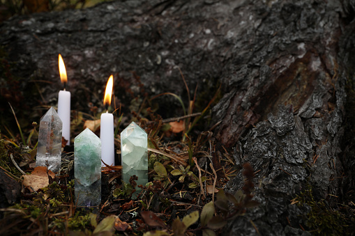 Different crystals and burning candles near tree outdoors, space for text