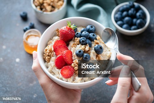 istock Oatmeal porridge bowl with berry fruits in female hands 1408374876