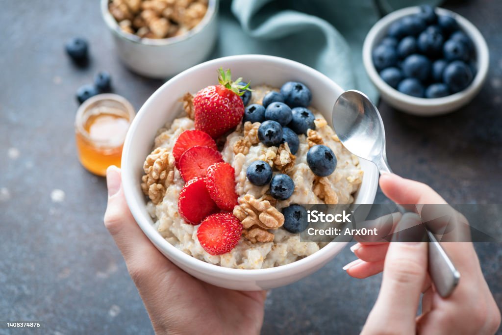 Oatmeal porridge bowl with berry fruits in female hands Oatmeal porridge bowl with berry fruits in female hands, closeup view. Healthy vegetarian breakfast food Oatmeal Stock Photo