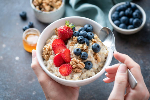 Oatmeal porridge bowl with berry fruits in female hands stock photo