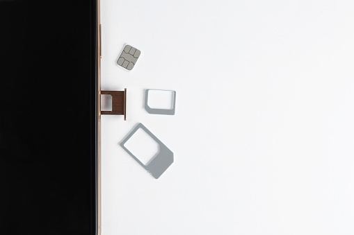 SIM card and mobile phone on white table, top view