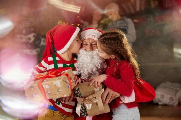 Cute little kids kissing Santa Clause after receiving Christmas presents at home.