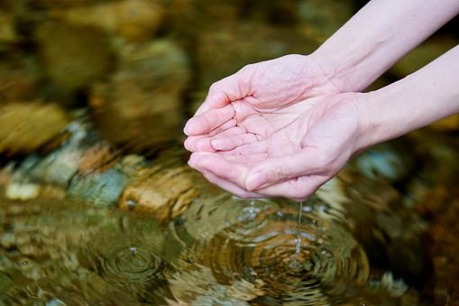 Hands of a woman saving river water