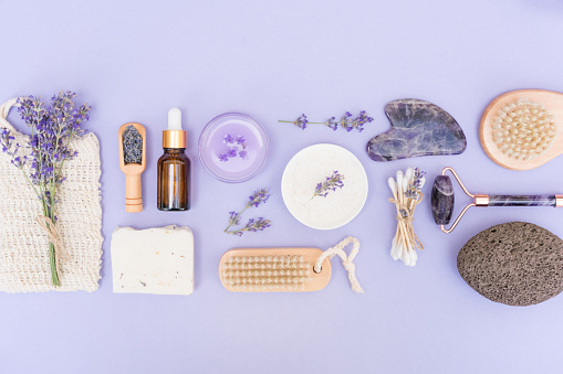 Natural bath accessories and self-care products for body and skin care over purple background with lavender flowers. Natural lavender cosmetics, eco living concept. Flat lay style