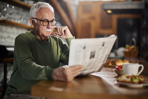 Mature man reading newspapers during morning time at home.