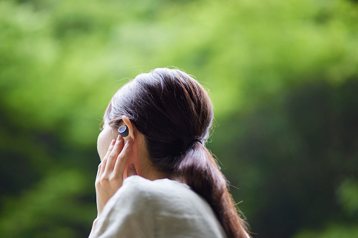 A young Japanese woman listening to music with wireless earphones in nature