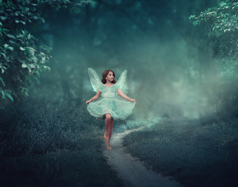 A girl with fairy wings runs through a fairy forest. Around the girl is a dark foggy forest. The girl has glitter wings.
She is dressed in blue