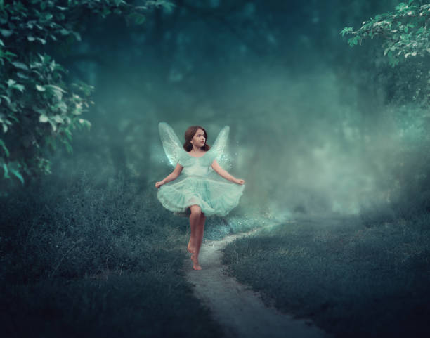a girl with fairy wings runs through a fairy forest. around the girl is a dark foggy forest. the girl has glitter wings.
she is dressed in blue - fairy forest fairy tale mist imagens e fotografias de stock
